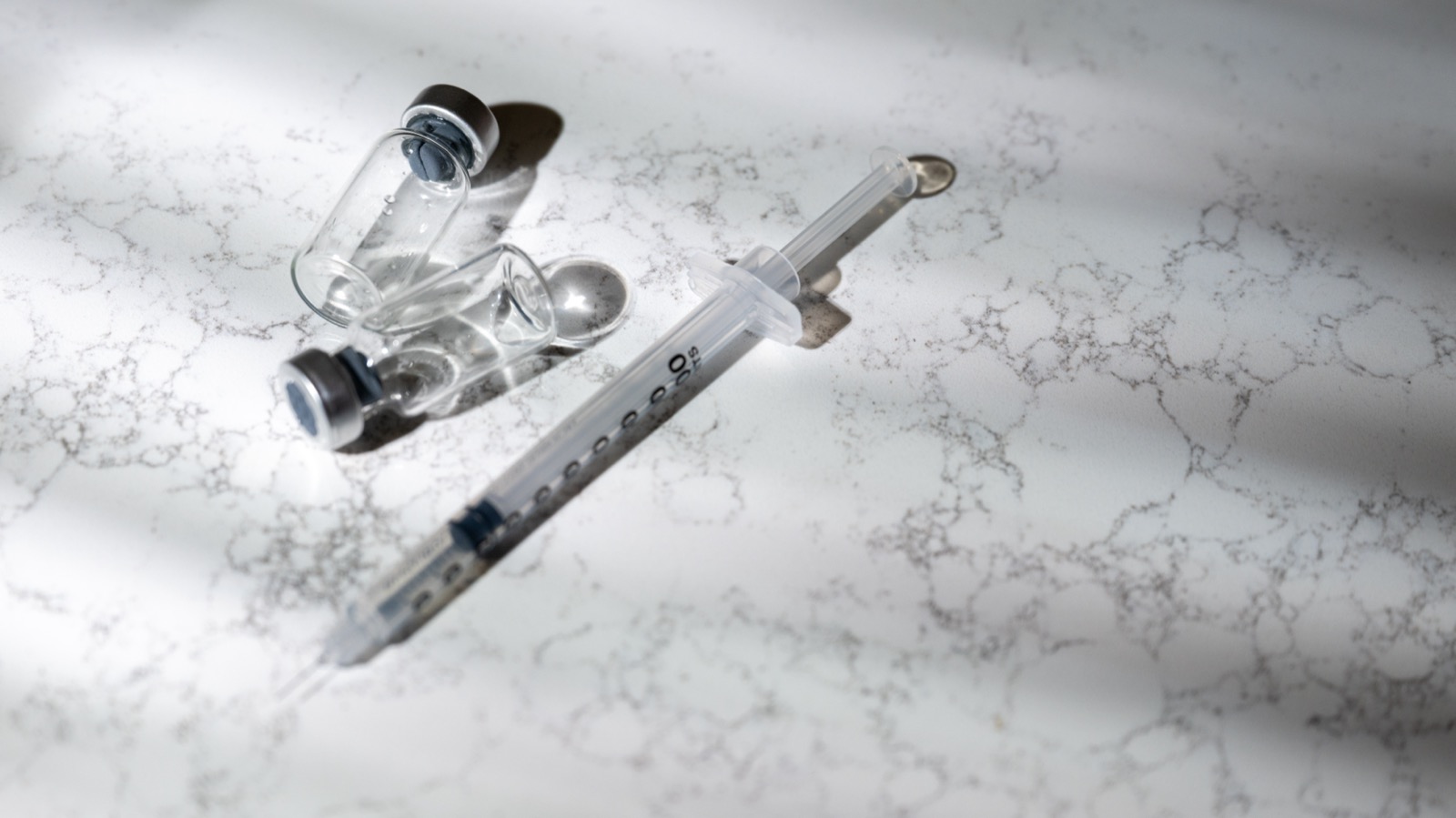 Vials and a syringe laid out on a marble kitchen counter, ready for self-injection