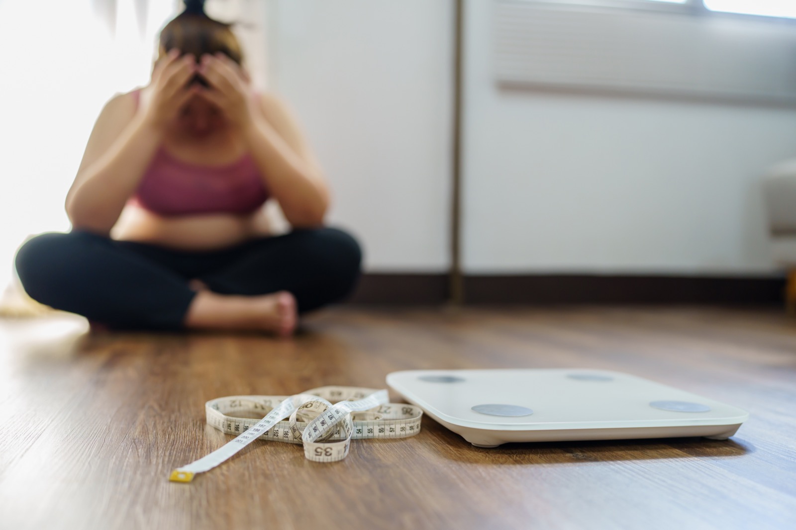 Woman sitting on the floor with her head in her hands, a scale and tape measure beside her