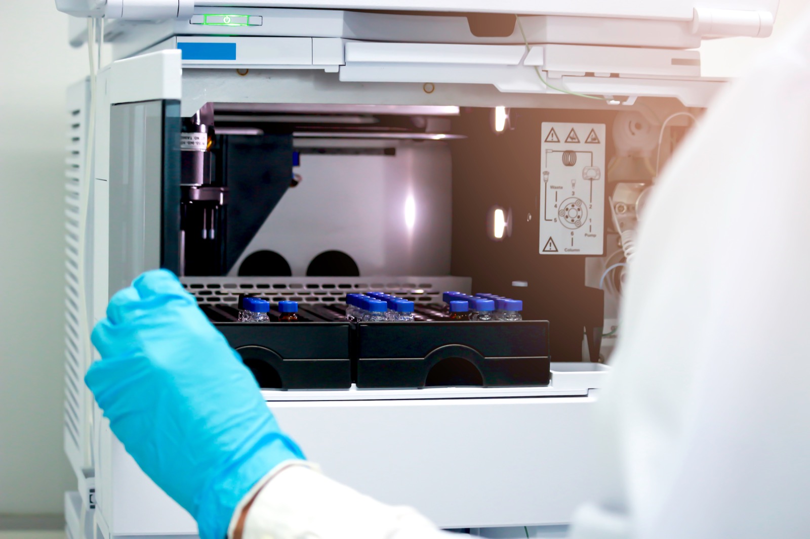 An HPLC laboratory instrument with rows of blue-capped sample vials loaded for analysis