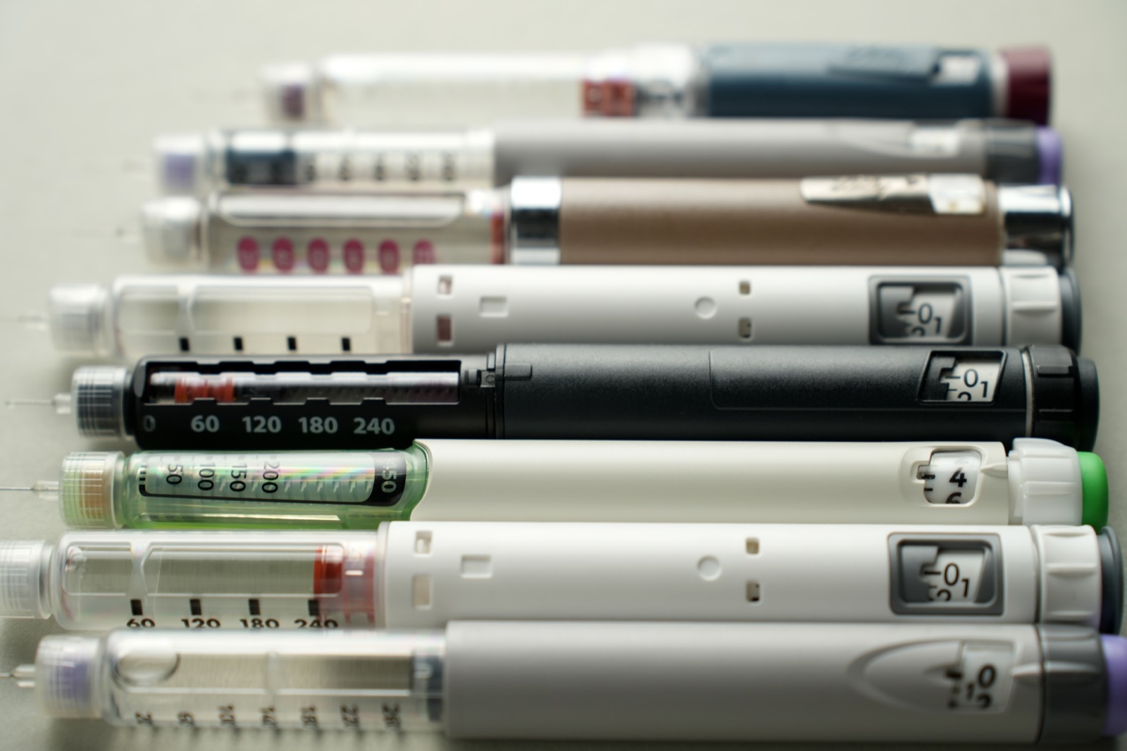 A row of different GLP-1 injection pen types laid side by side, illustrating the variety of devices patients must navigate
