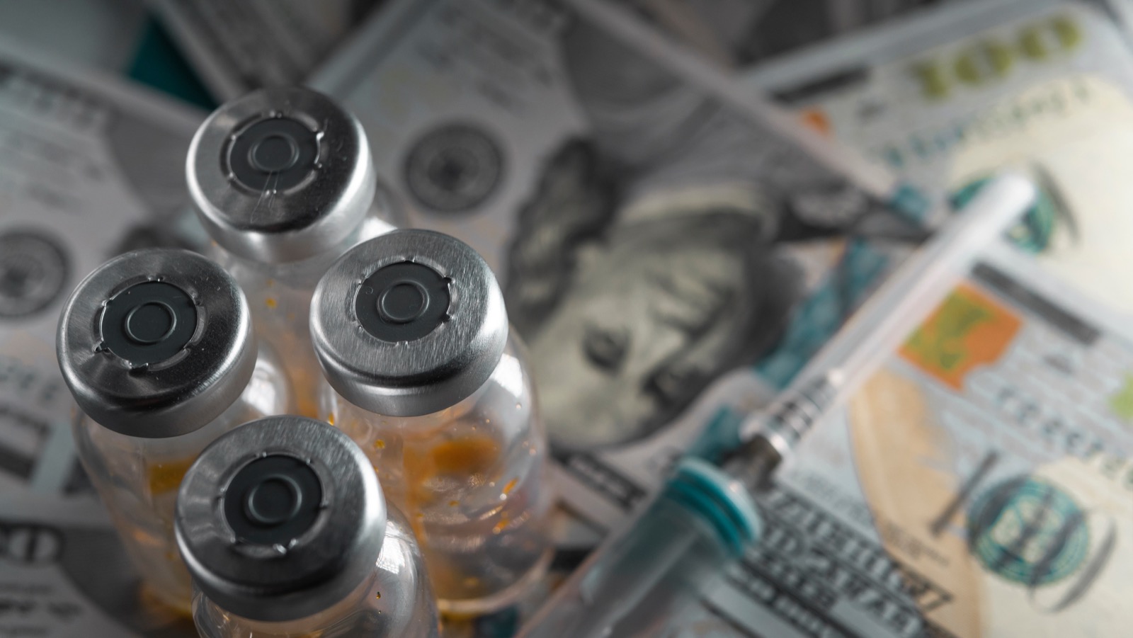 Vials of injectable medication sitting on top of hundred-dollar bills, illustrating the profit margins of gray-market peptides